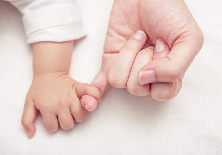 Mano de una madre que, con el dedo meñique coge el dedo meñique de la mano de su bebé